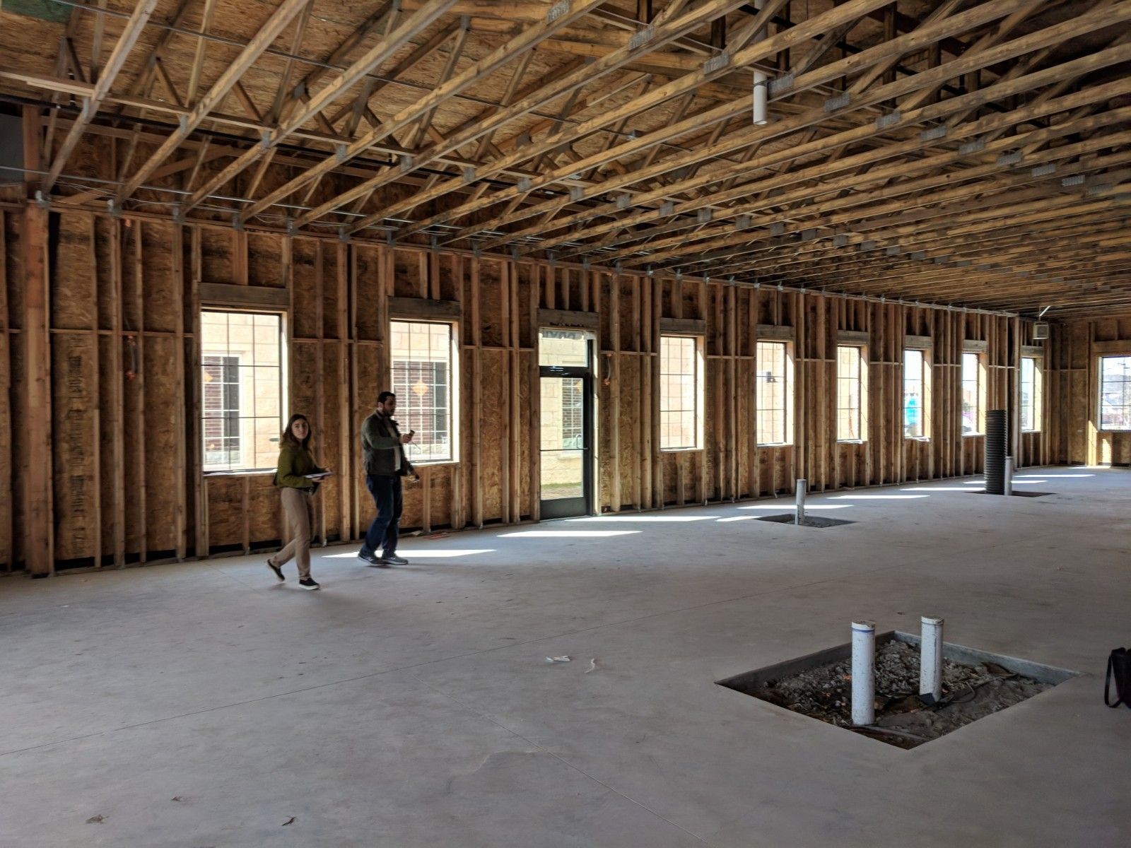 Two people walking inside a large unfinished building with exposed wooden beams and framework.